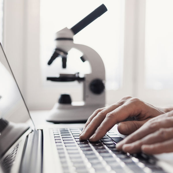 person on laptop with microscope in background